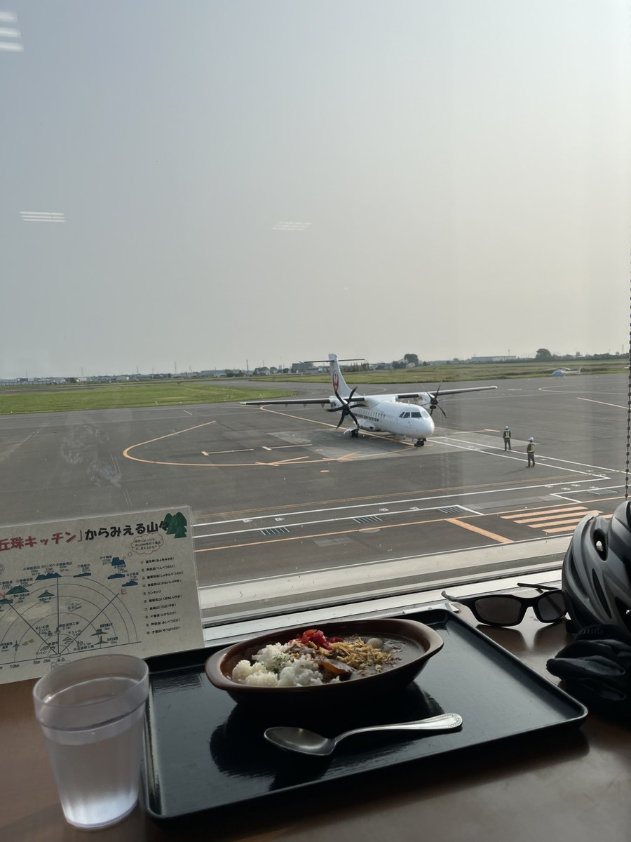 丘珠空港の滑走路に駐機するプロペラ機と、テーブルの上の丘珠ミニカレー