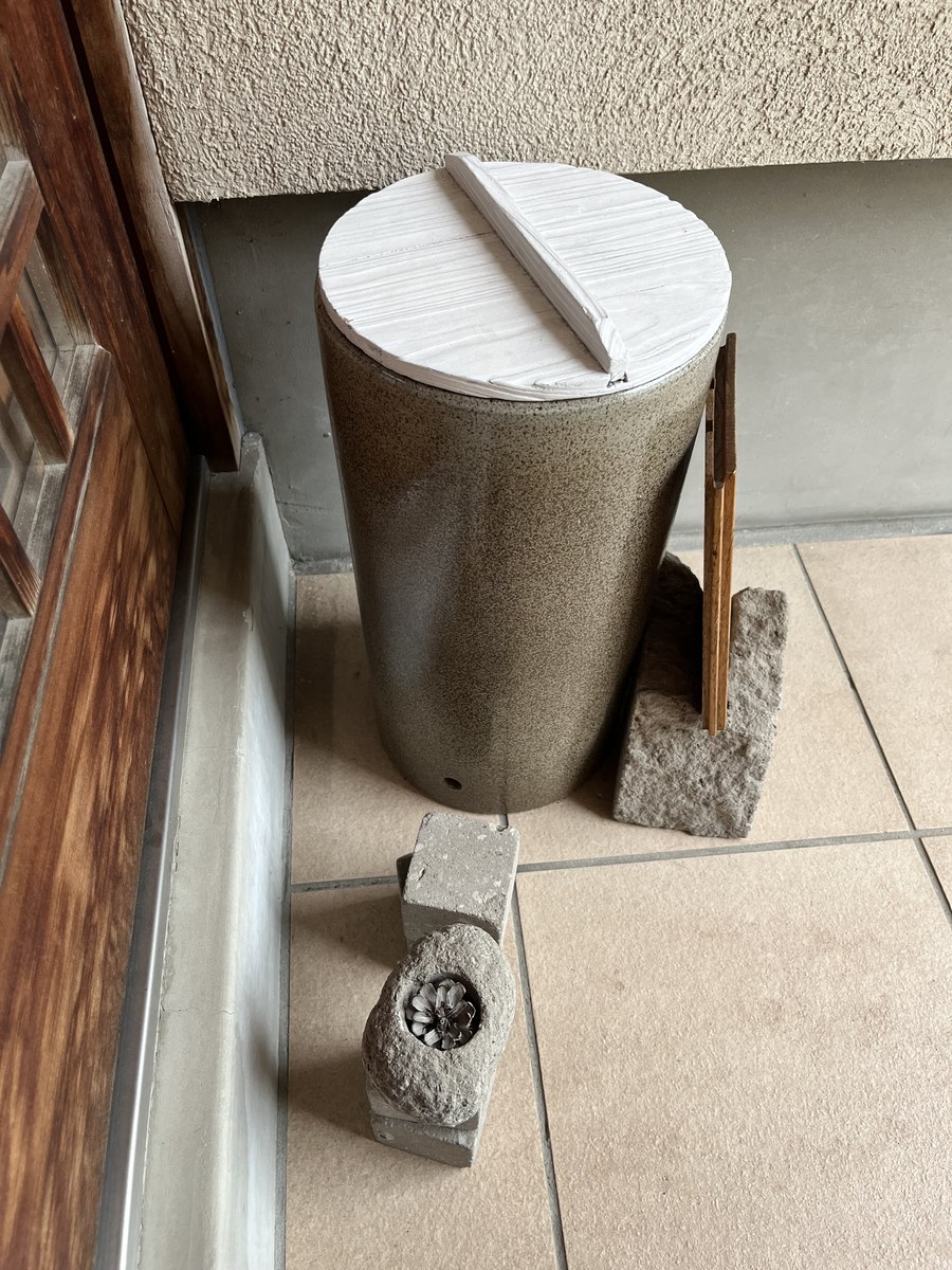 陶器の傘立てに載せた、白くペイントした木製の鍋ぶた